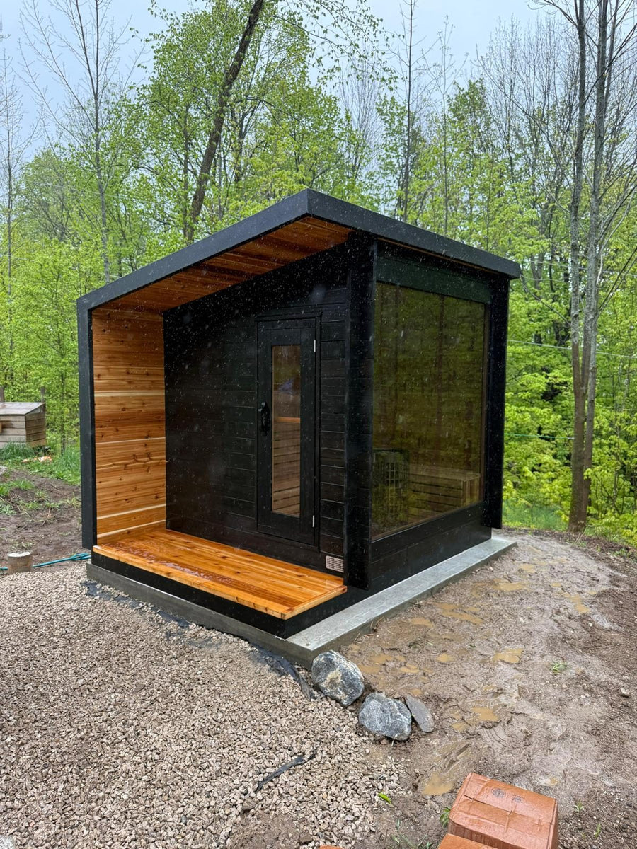 The same sauna model set on gravel at the edge of a spring forest
