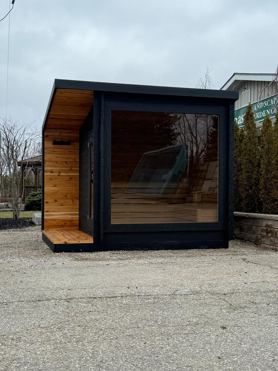 The sauna outdoors on a gravel pad, its glass wall reflecting the trees